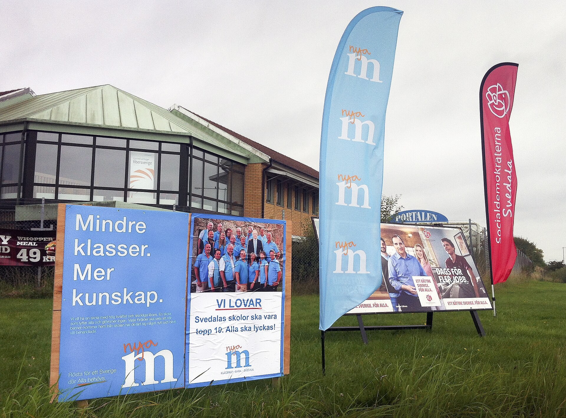 Moderaternas och Socialdemokraternas valaffischer och flaggor på en gräsmatta i Svedala.