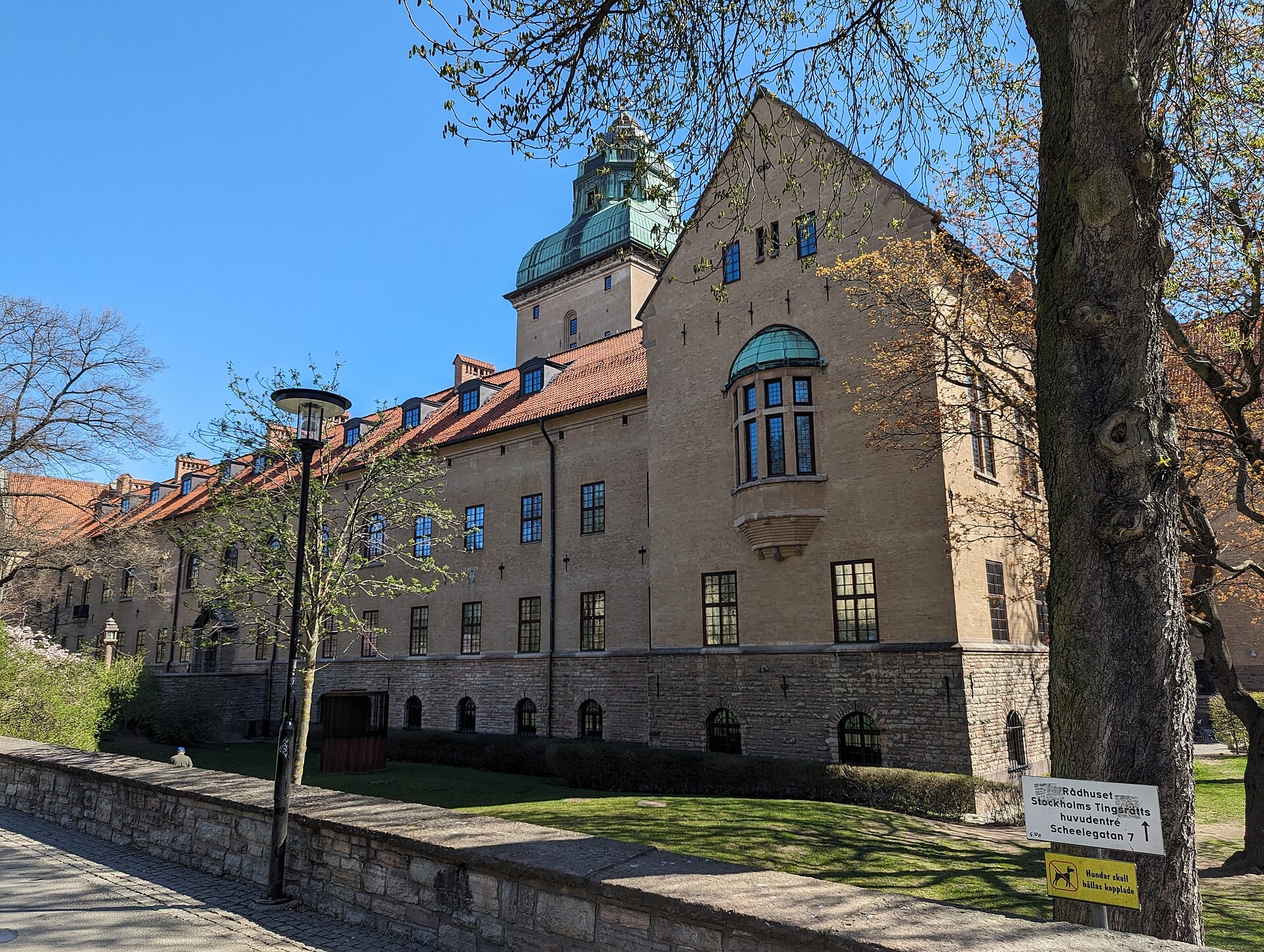 Stockholms tingsrätts byggnad med tegeltak och torn, sedd från en trädgård.