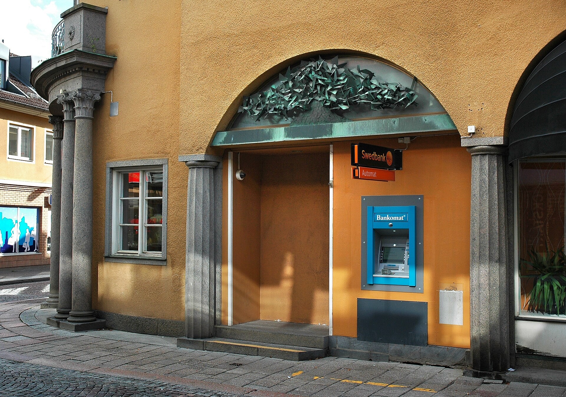 En blå bankomat i en gul husfasad med en Swedbankskylt ovanför.