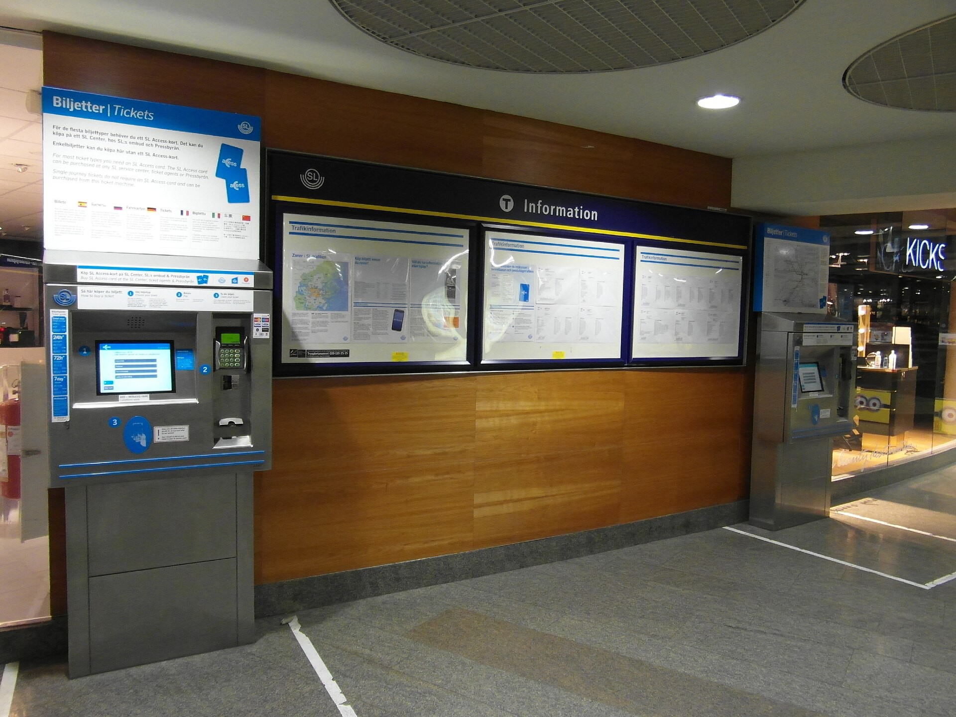 Två biljettautomater på var sin sida om SL:s informationstavla i en stationshall.