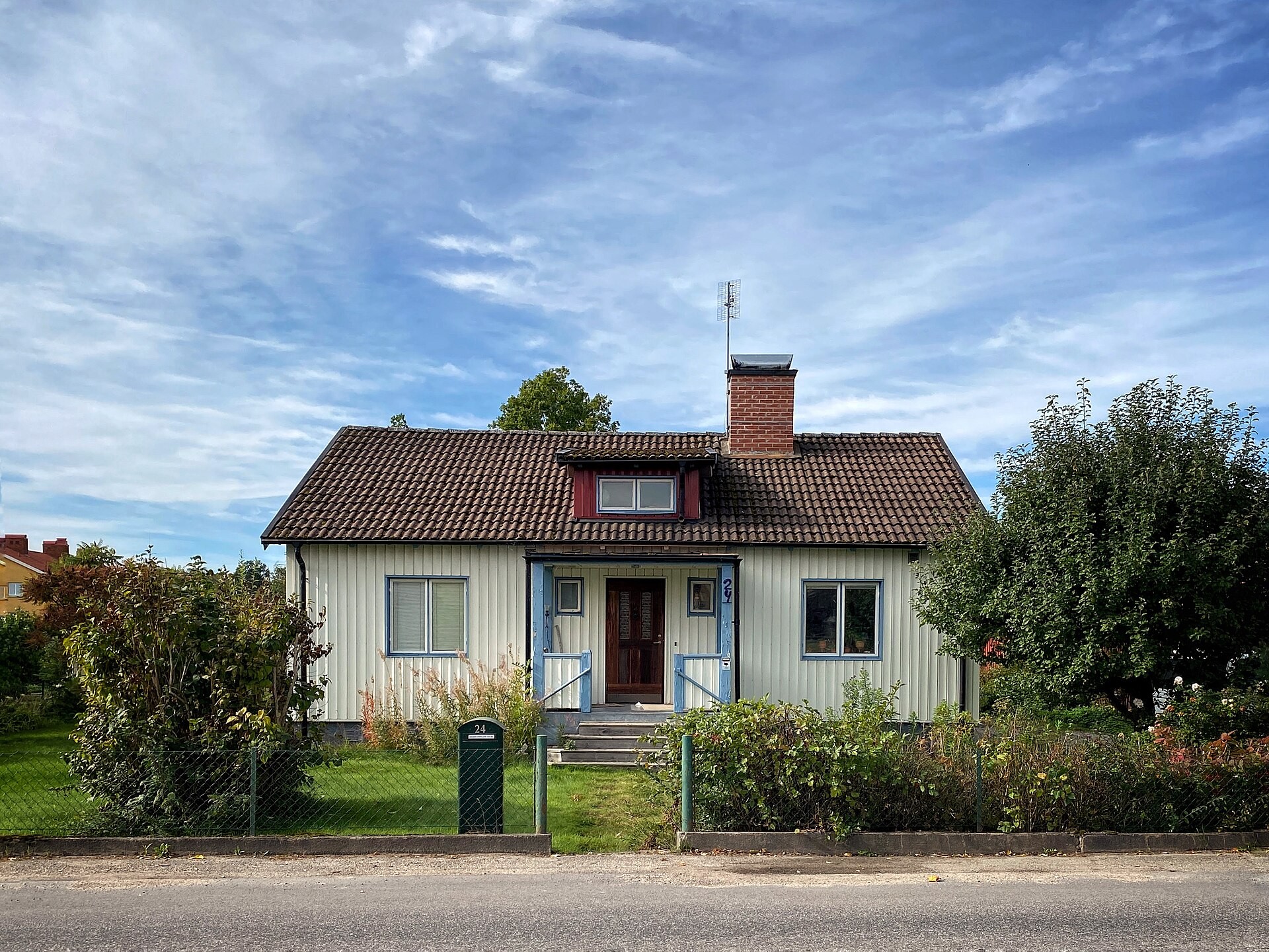 En ljus villa med tegeltak och en trädgård bakom ett grönt staket.