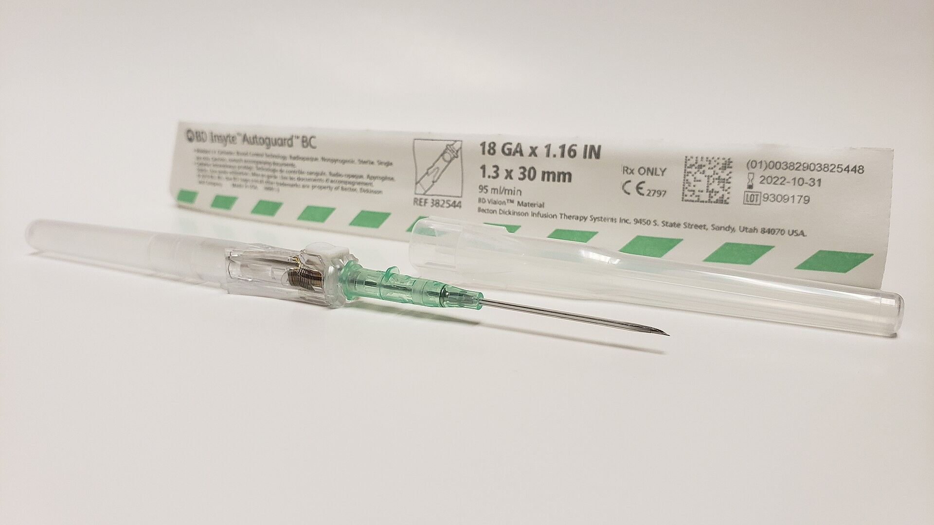 En intravenös kateter med nål ligger framför en förpackning på en vit yta.